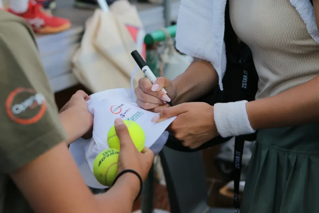 Una giocatrice firma una pallina da tennis per i tifosi all’Open delle Puglie.